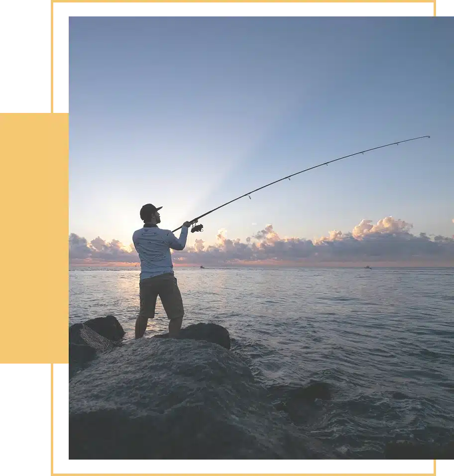 Man fishing on rocks at sunrise.